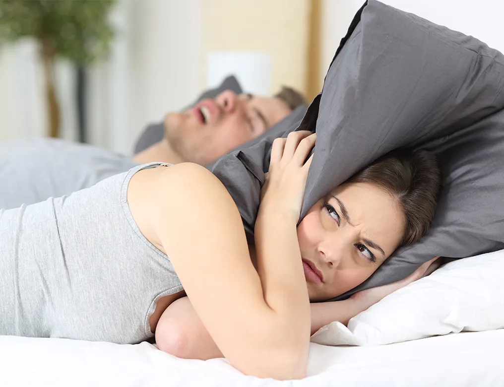 Man in woman in bed with man snoring and woman annoyed